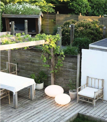 Une terrasse en bois élégante et paisible, agrémentée de mobilier d’extérieur blanc et de deux lampes rondes posées au sol diffusant une lumière douce.