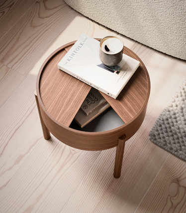 Table d'appoint ronde Woud en bois chaleureux avec plateau décalé et tiroir ouvert. Un livre Kinfolk et une tasse de café reposent sur la table, sur un socle en bois clair.