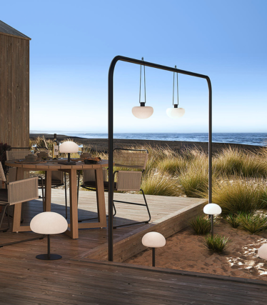 Luminaires d'extérieur sur une terrasse en bois au bord de la mer, lumière douce entre les herbes des dunes.
