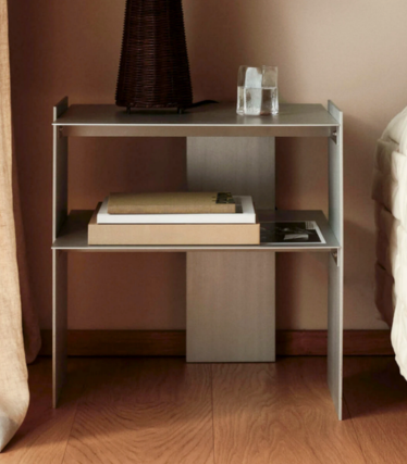 Table de chevet étroite en métal avec deux étagères, des livres, un verre et un vase à côté d'un lit.
